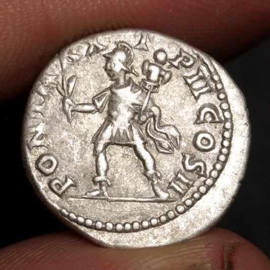 An ancient silver coin featuring a standing figure, held between fingers against a dark background.