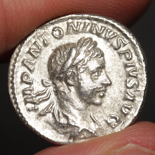 ancient silver coin with bust of young man, being held between two fingers against a dark background