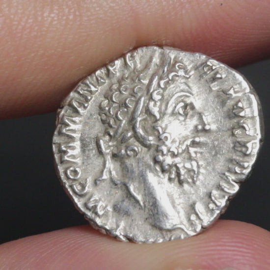 an ancient silver coin being held between two fingers and rotated to show both sides