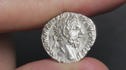 an ancient silver coin being held between two fingers and rotated to show both sides