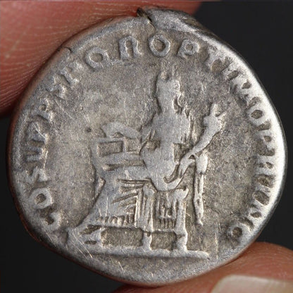 Ancient Roman silver coin held between fingers with dark background