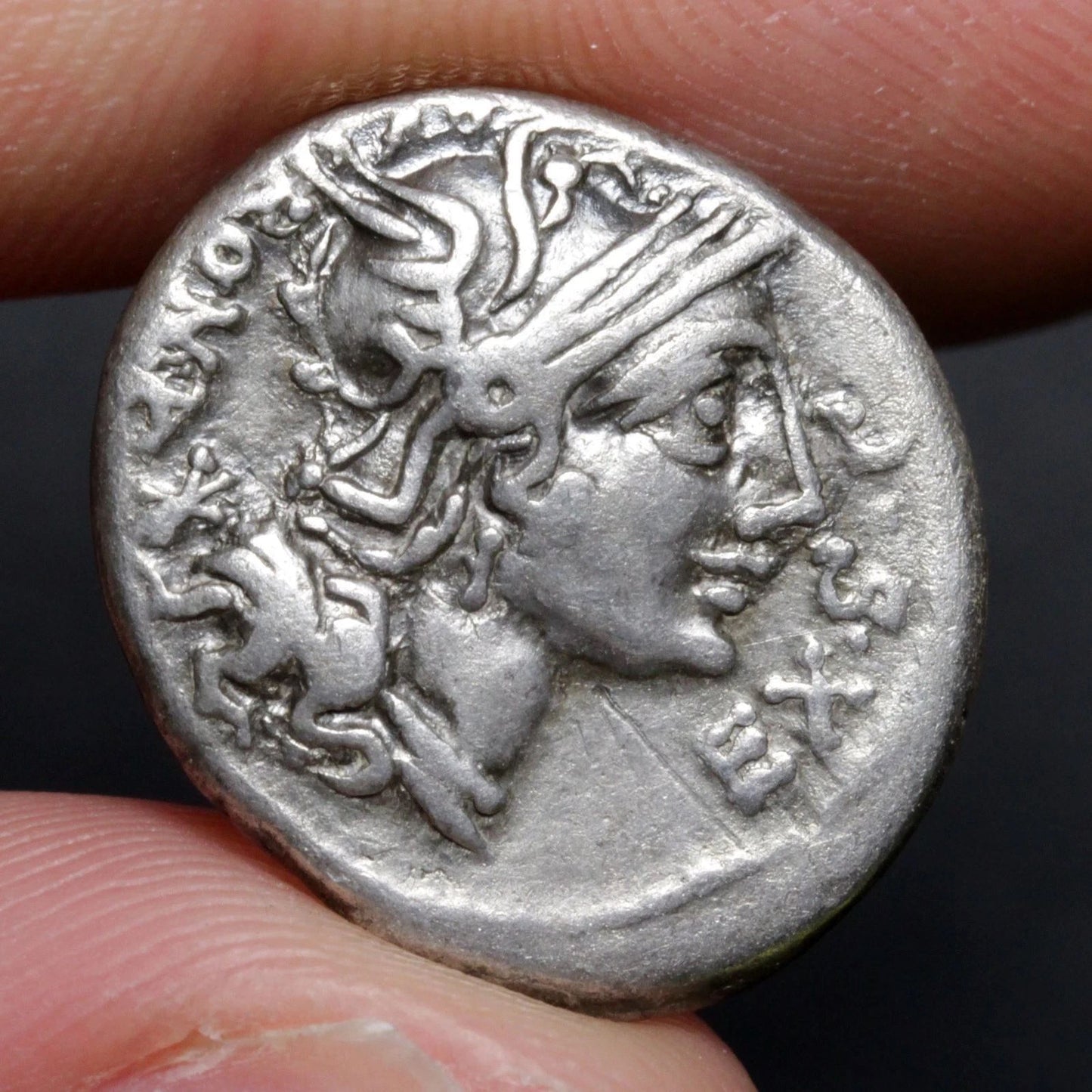 Ancient silver coin with a profile of a person and eagle, held between fingers.