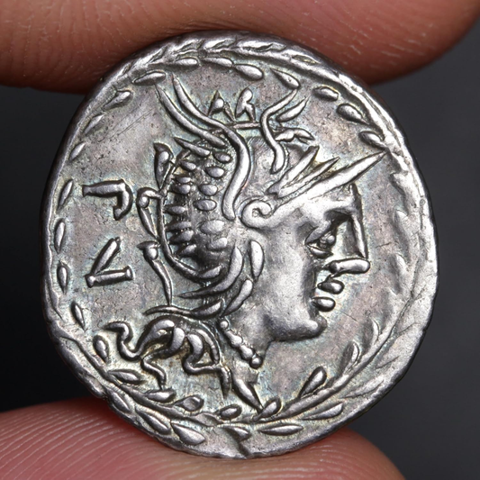 An ancient silver coin featuring a profile portrait of a woman with a laurel wreath, held between fingers against a dark background.