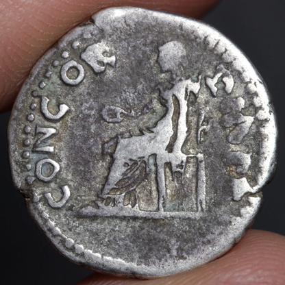 denarius coin with seated figure being held between two fingers