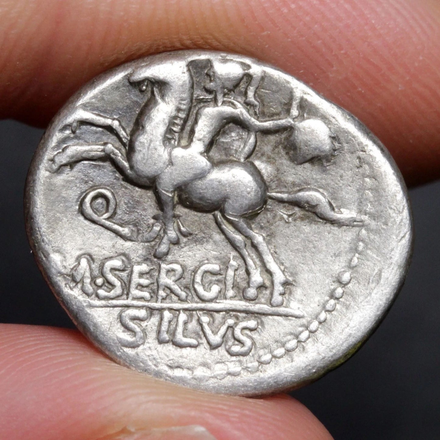 Ancient silver coin with a Pegasus design held between fingers