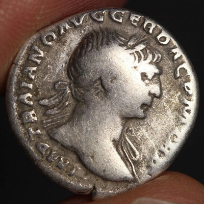 Ancient Roman coin with a profile of a emperor held by a hand against a dark background